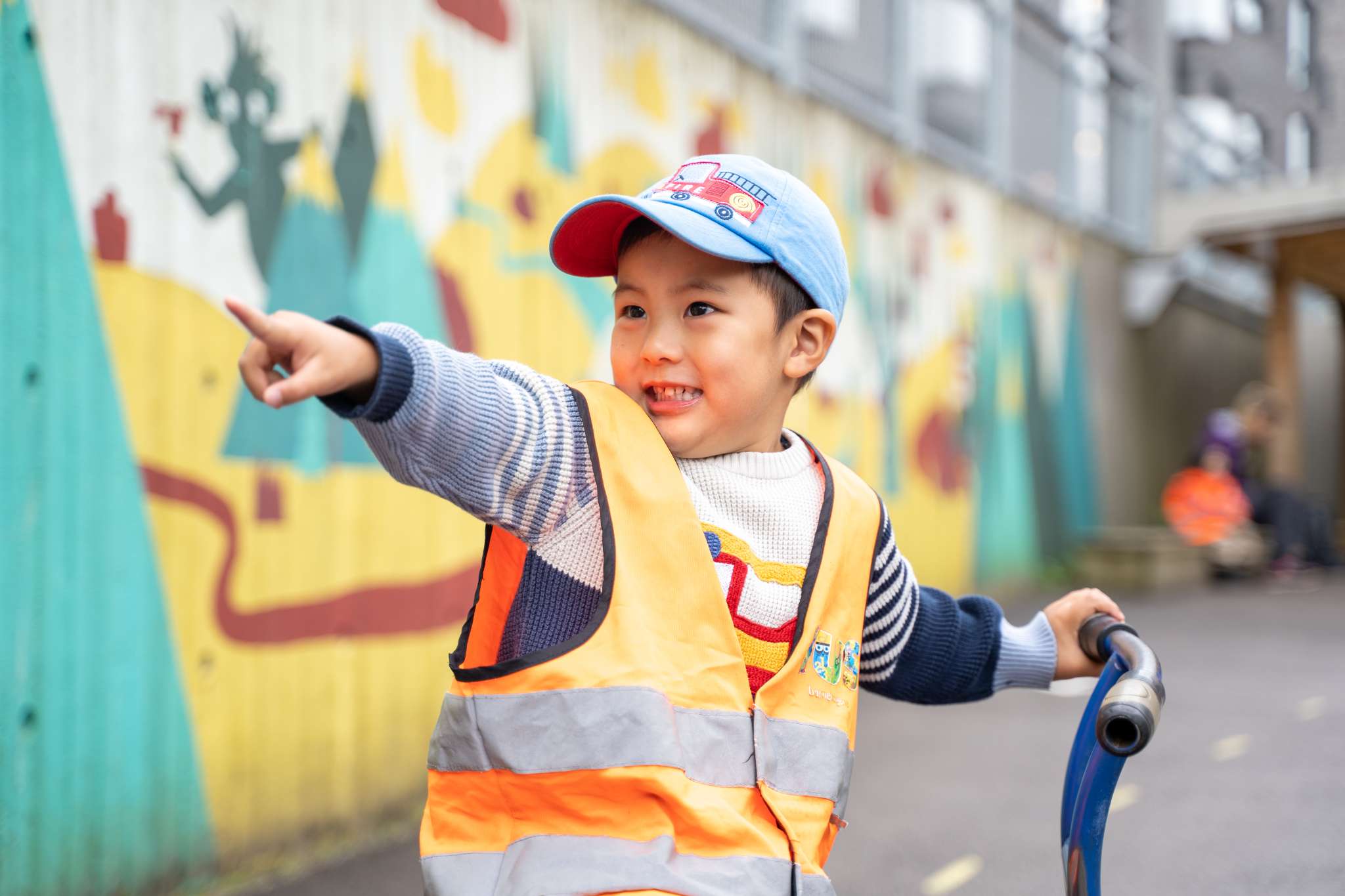 Barnehagegutt med caps og gul vest peker, foto