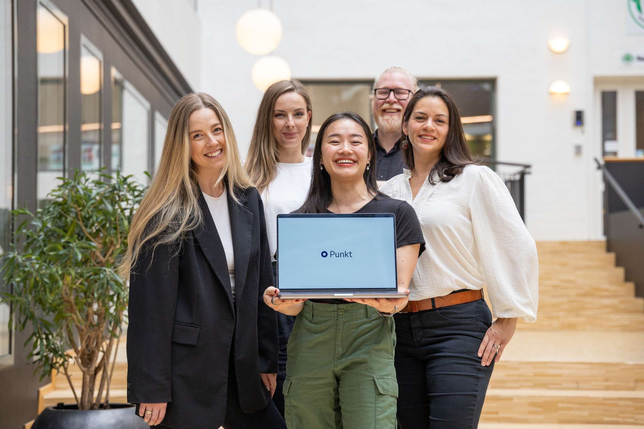 Fire kvinner og en mann holder fram en datamaskin som viser fram designsystemet Punkt. Foto.