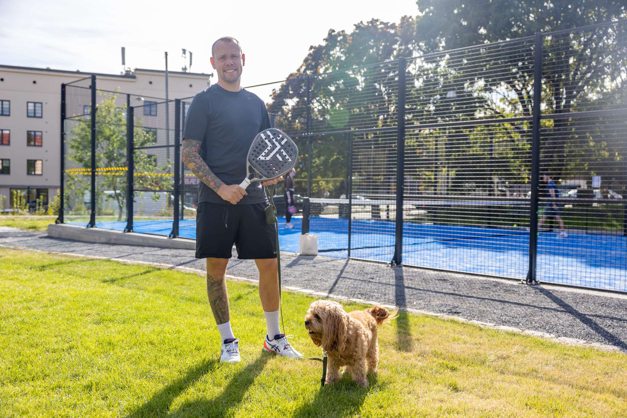 Smilende mann står utenfor en padelbane. Foto.