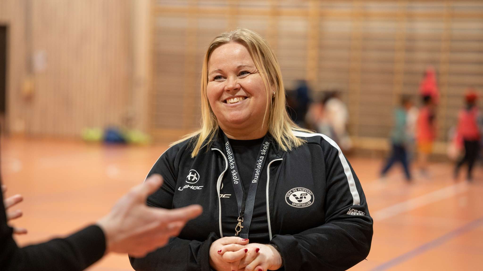 Smilende kvinnelig trener i en gymsal. Foto.