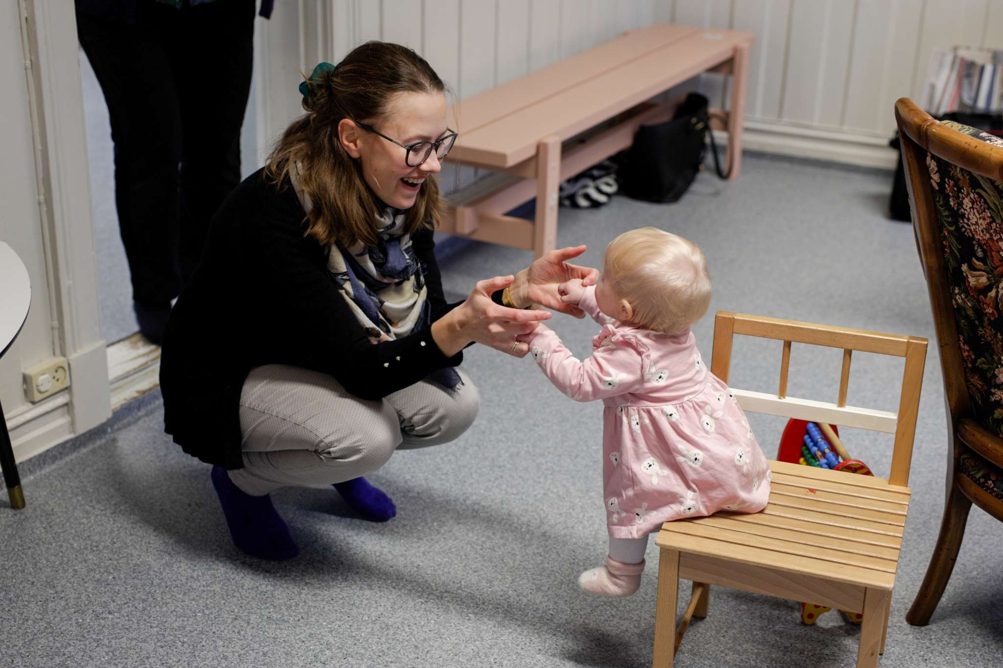 Kvinne leker med barnet sitt som sitter på en stol. Foto.