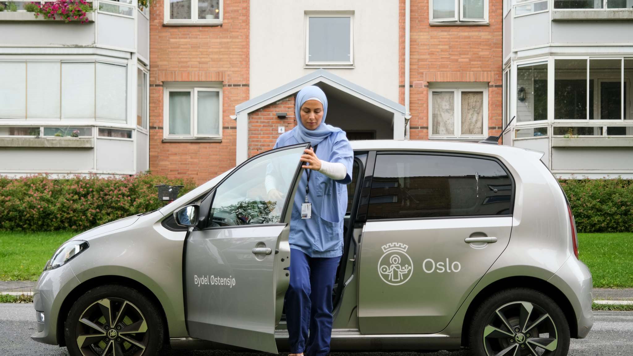 Kvinne på jobb i hjemmesykepleien går ut av bilen sin. Foto.