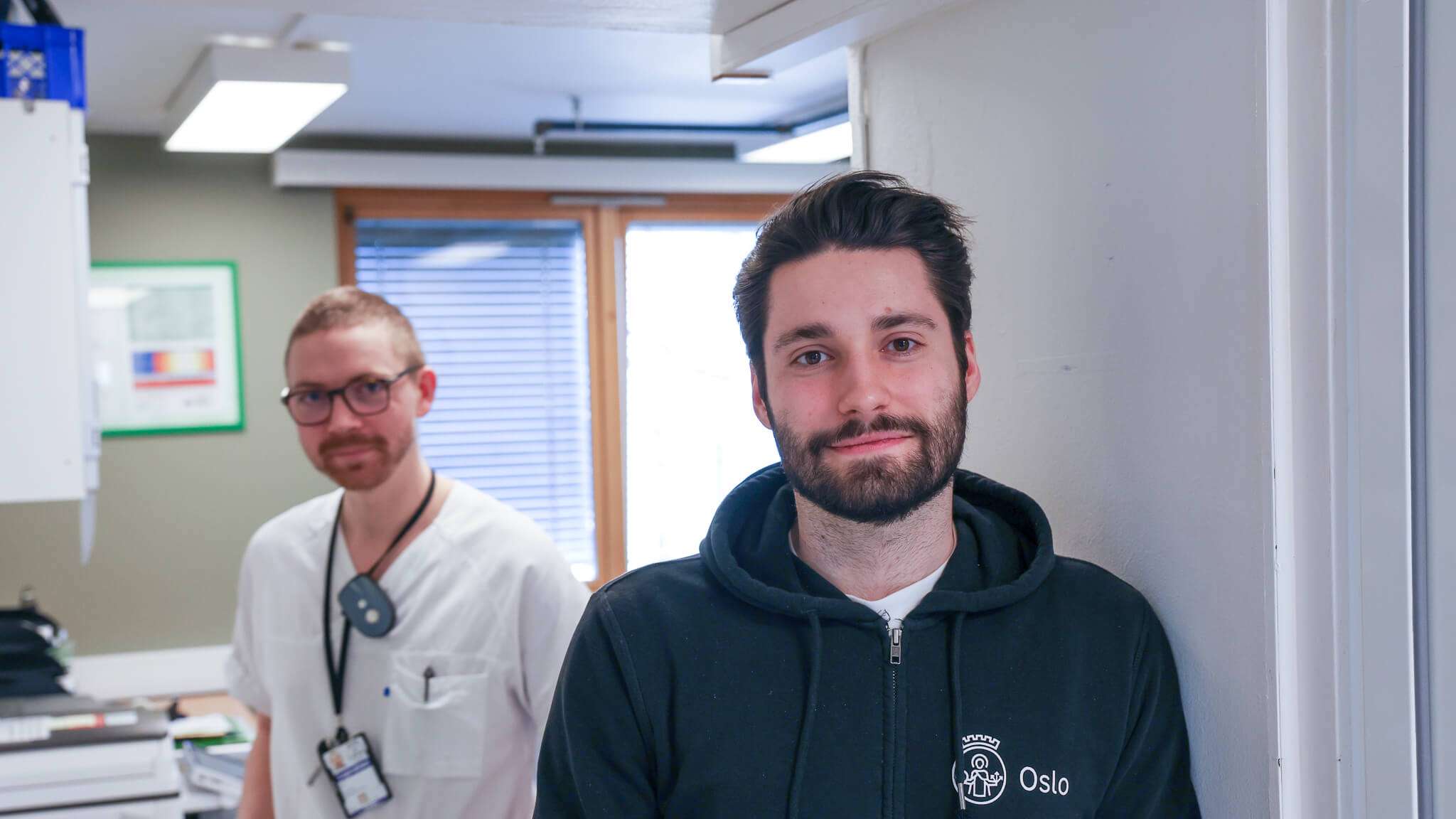 En sykepleier og en utvikler ser i kamera på legevakta, foto