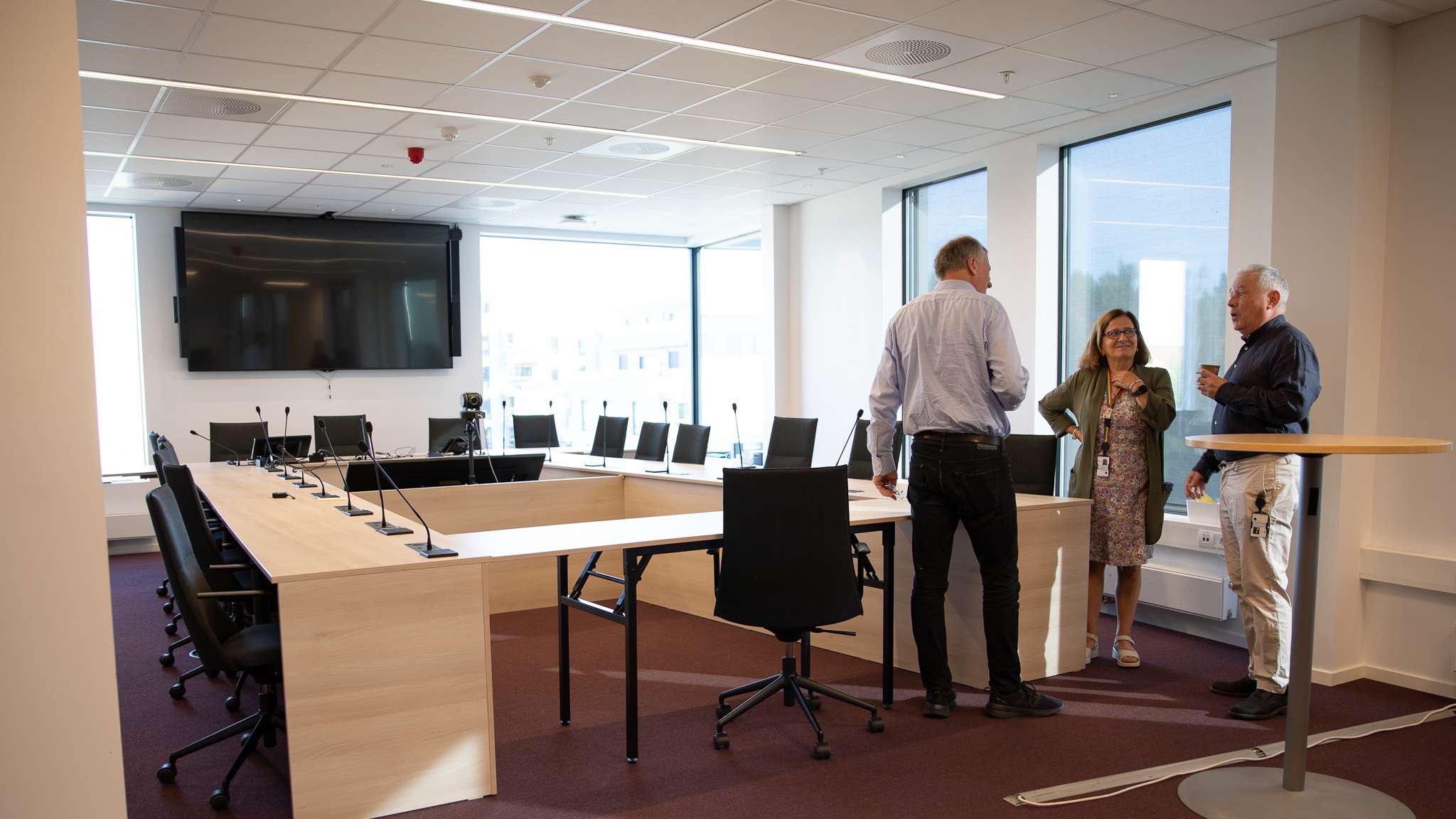 To menn og en kvinne snakker sammen i et stort, moderne møterom. Foto.