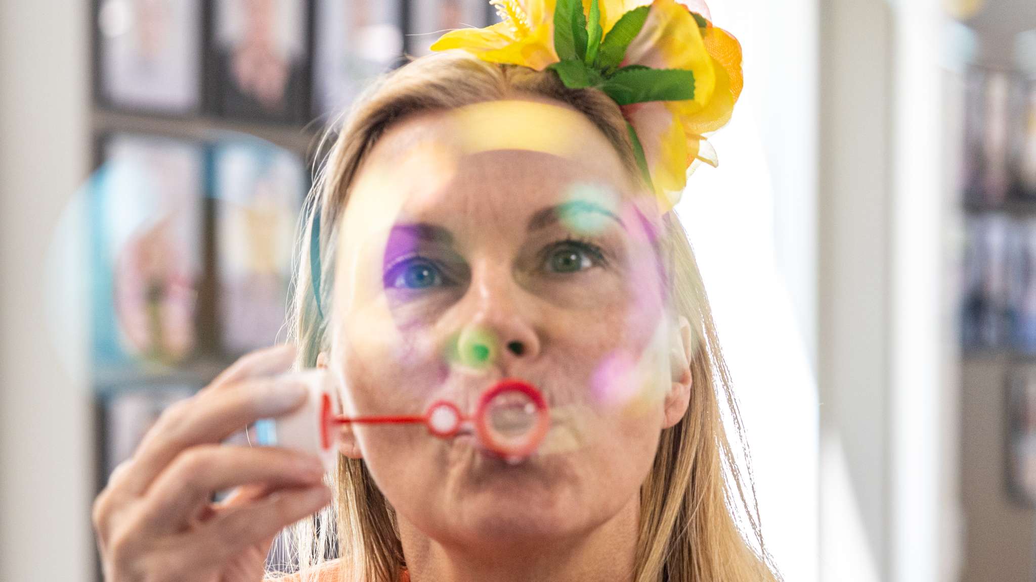 Kvinne er innendørs og blåser såpebobler med blomst i håret.