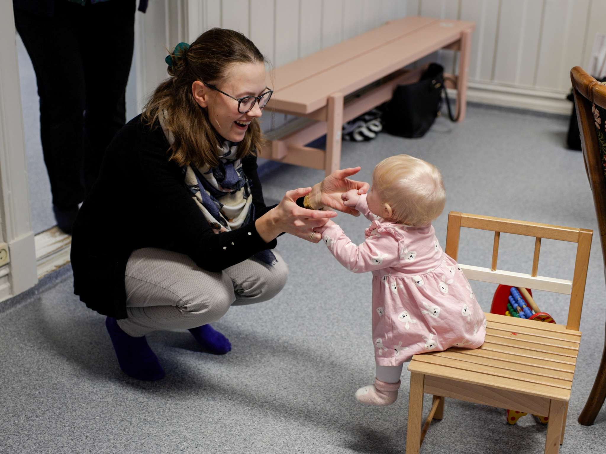 Kvinne leker med barnet sitt som sitter på en stol. Foto.