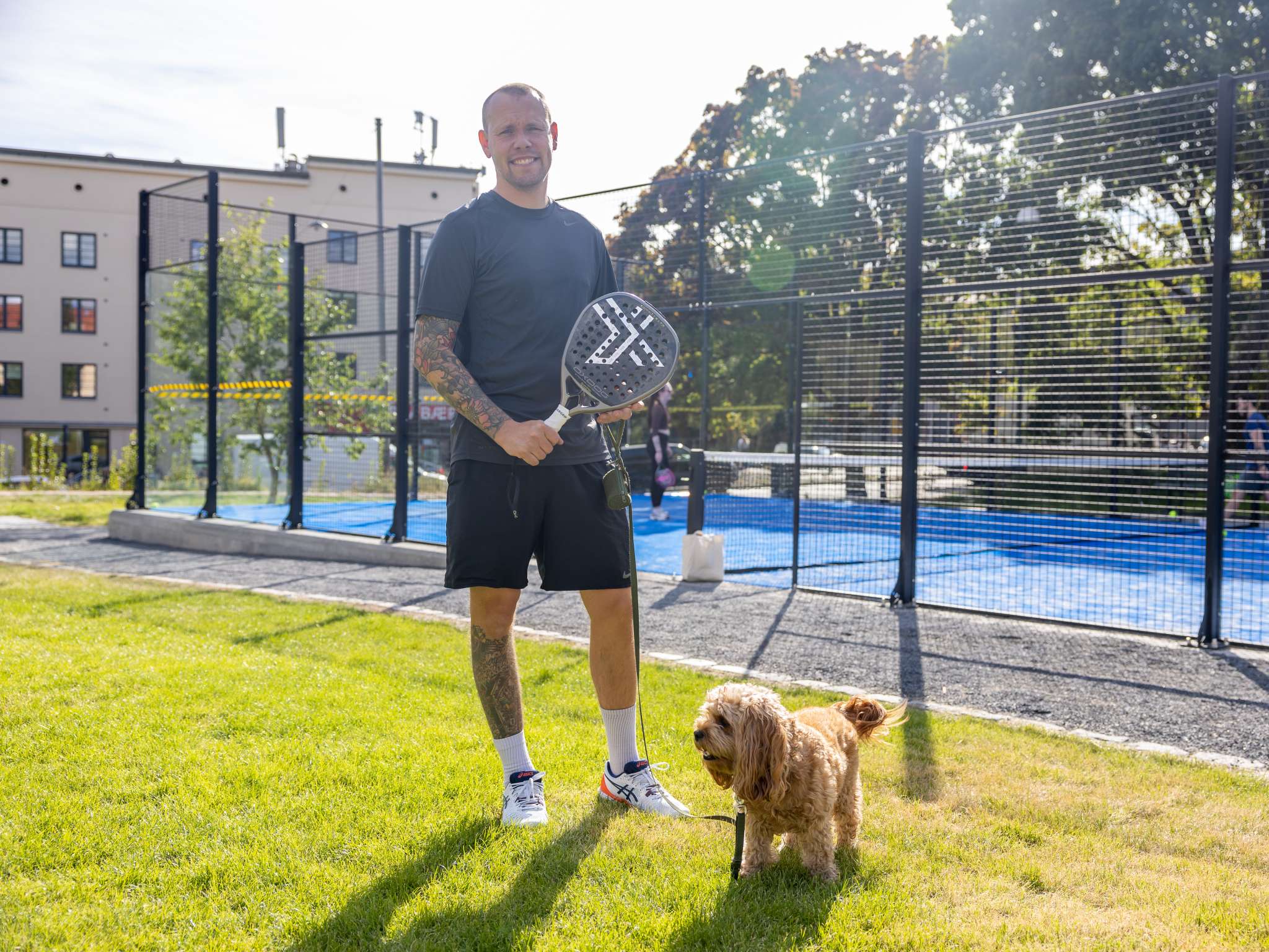 Smilende mann står utenfor en padelbane. Foto.