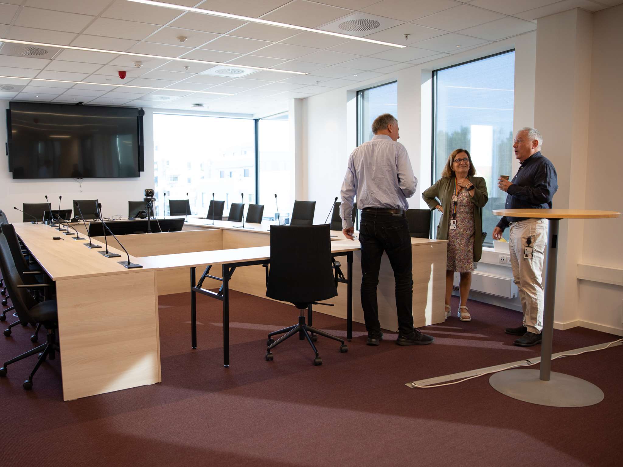 To menn og en kvinne snakker sammen i et stort, moderne møterom. Foto.