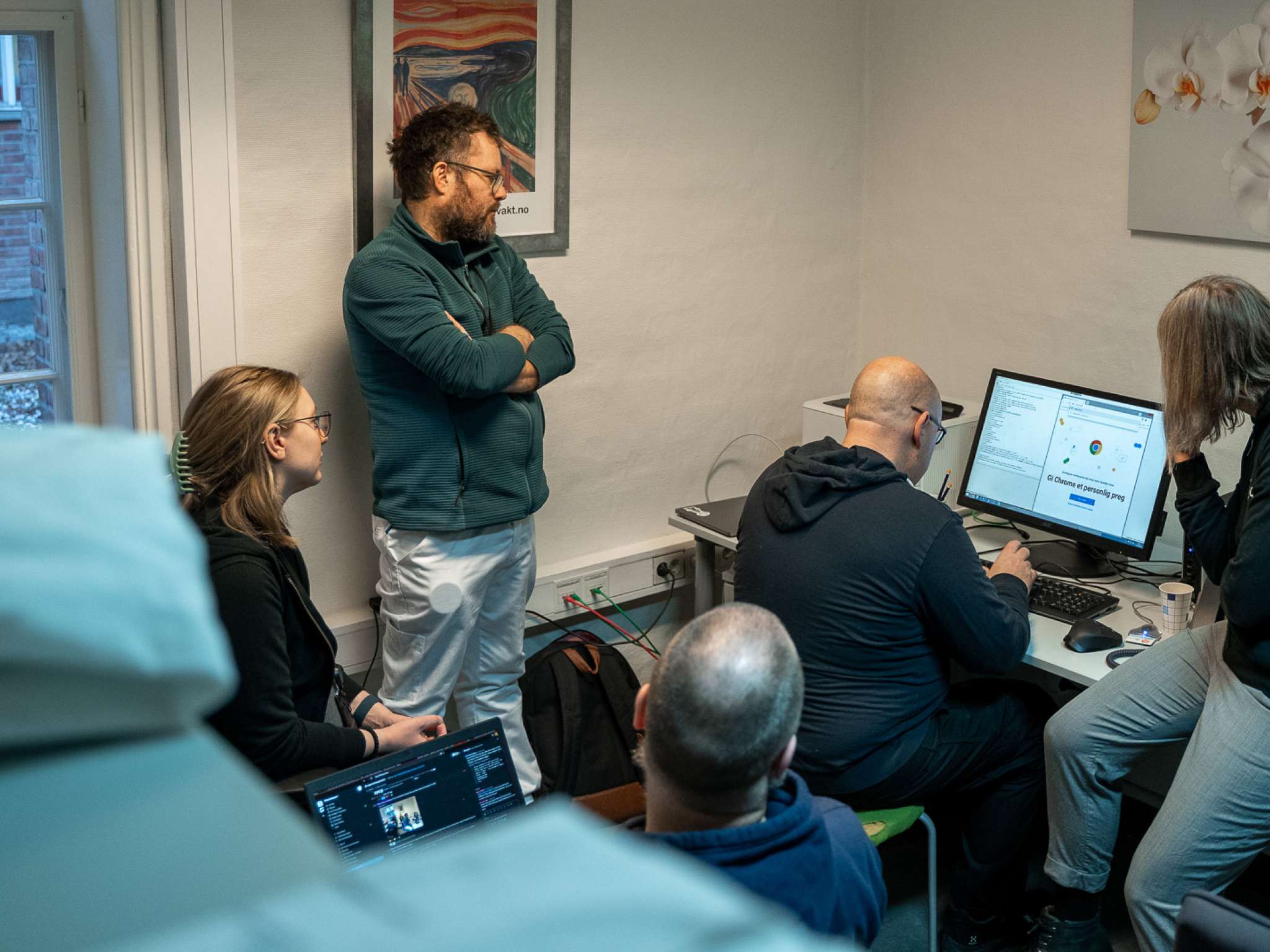 En lege ser på en gruppe utviklere som programmerer på en datamaskin. Foto.