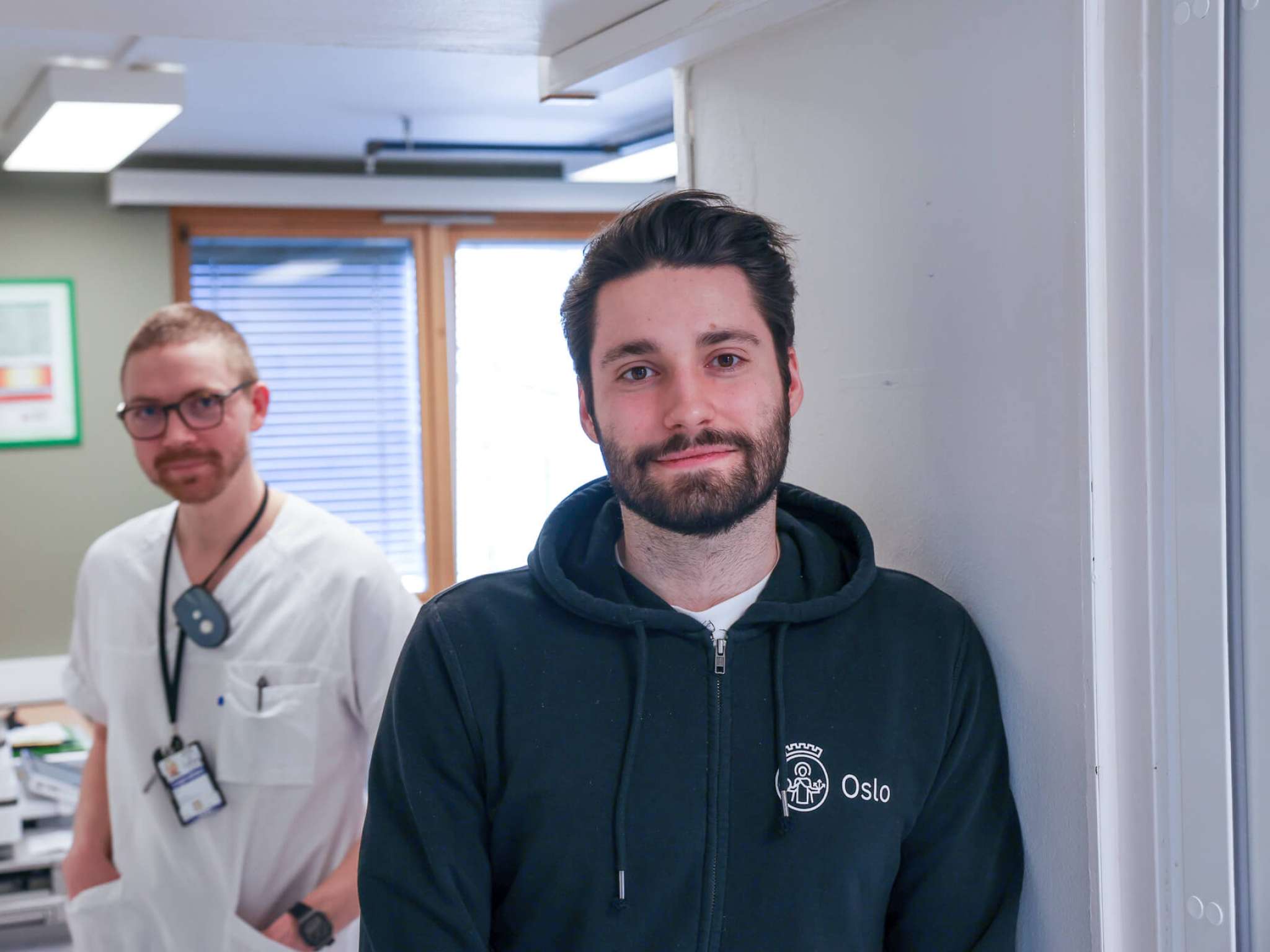 En sykepleier og en utvikler ser i kamera på legevakta, foto