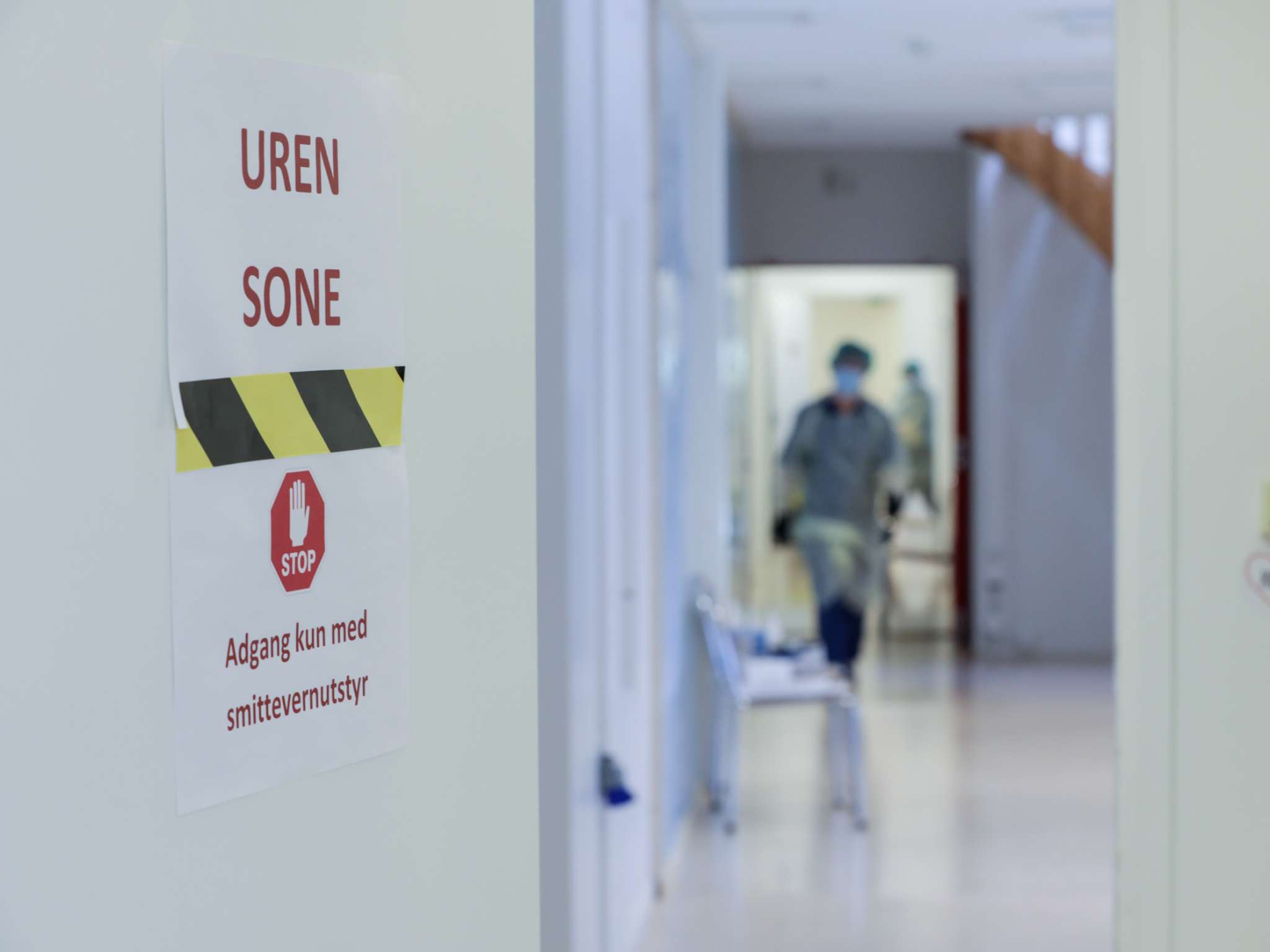 Helsearbeider i smittevernutstyr i en trappeoppgang, innenfor en dør med skiltet "Uren sone - adgang kun med smittevernutstyr"