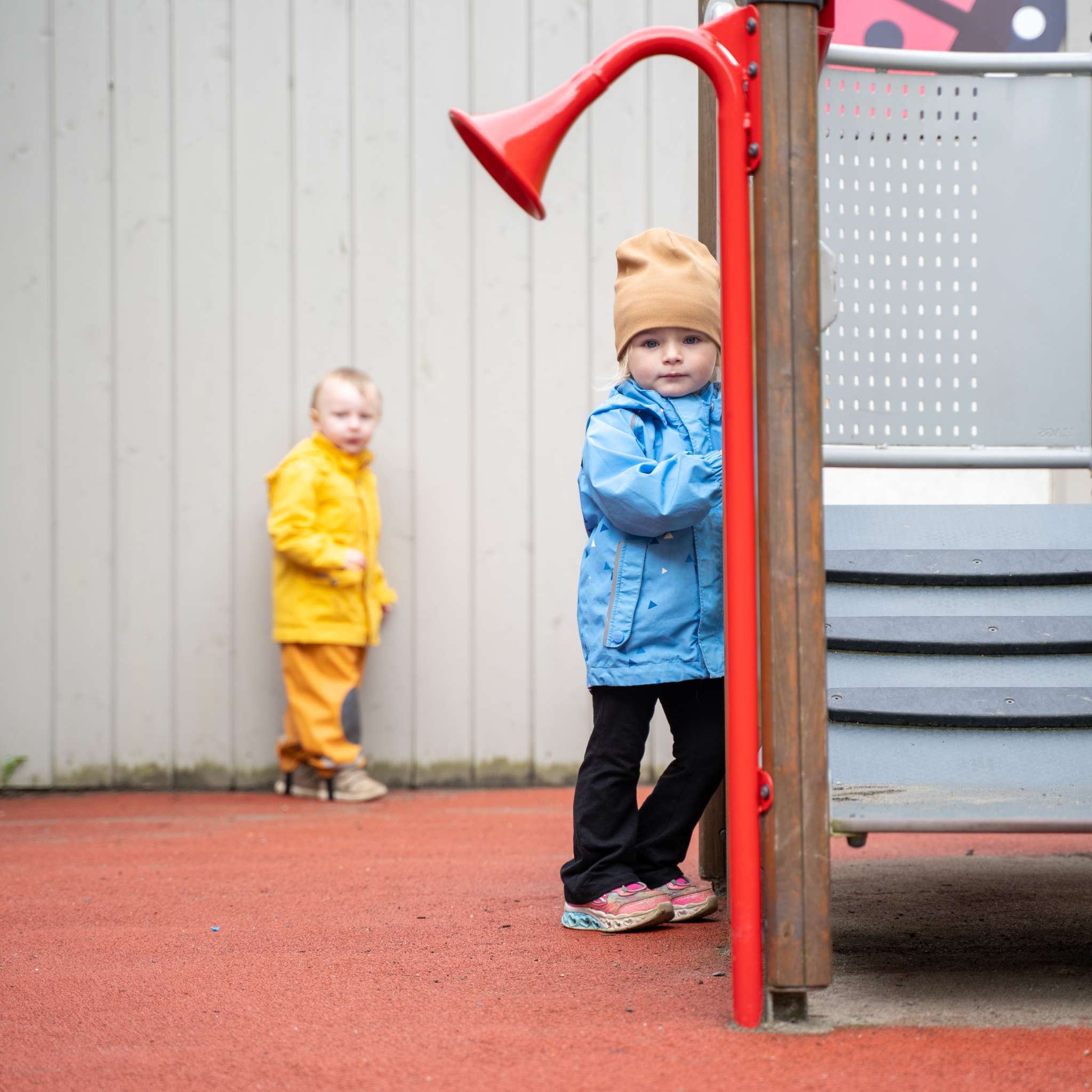 To barn i uteklær står ved siden av et lekestativ, foto