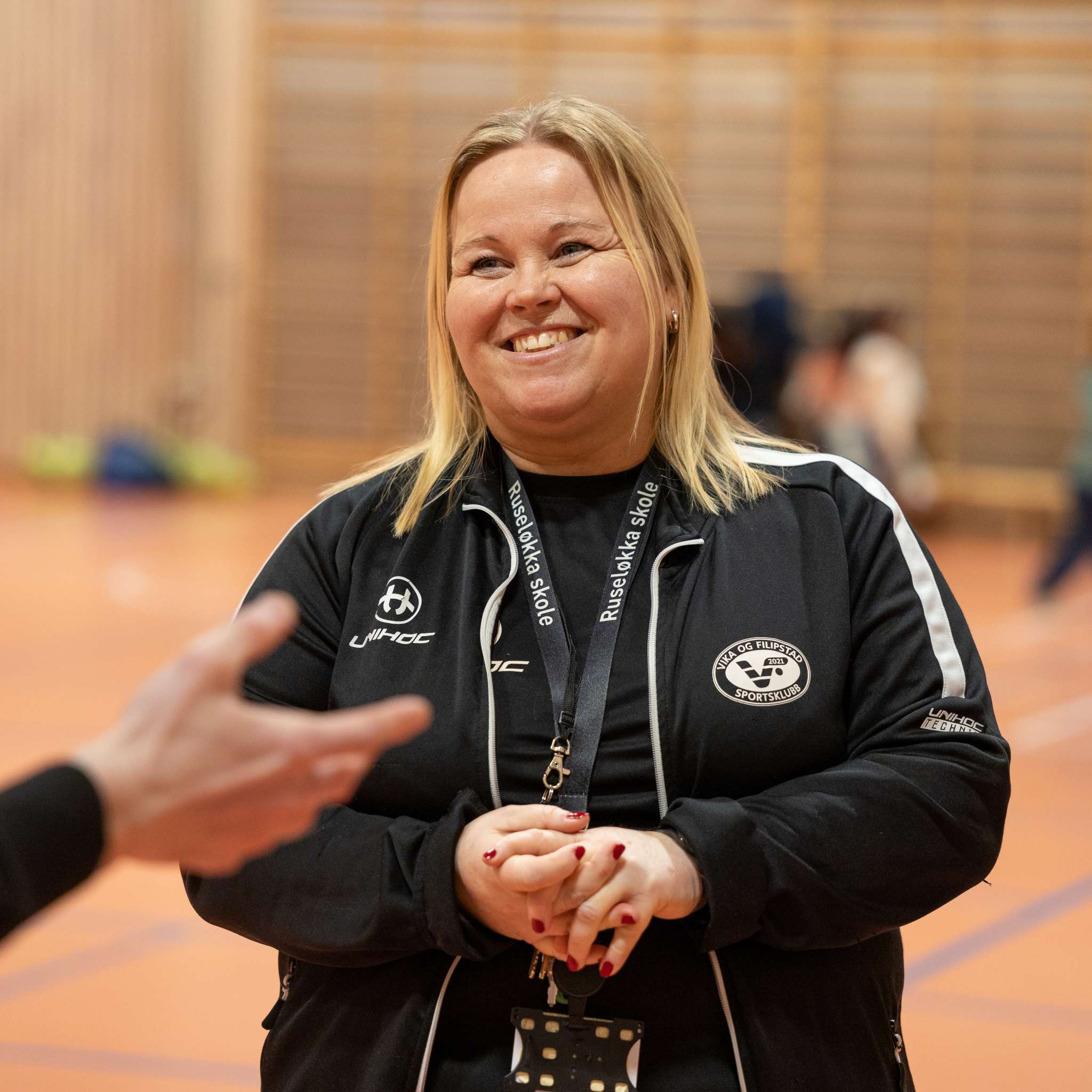 Smilende kvinnelig trener i en gymsal. Foto.