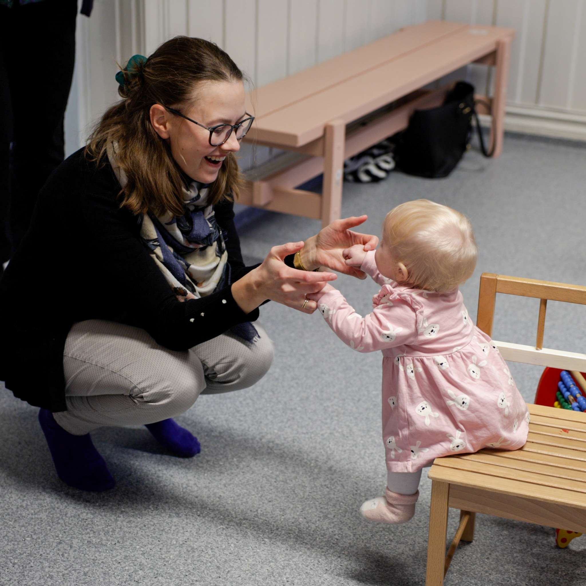 Kvinne leker med barnet sitt som sitter på en stol. Foto.