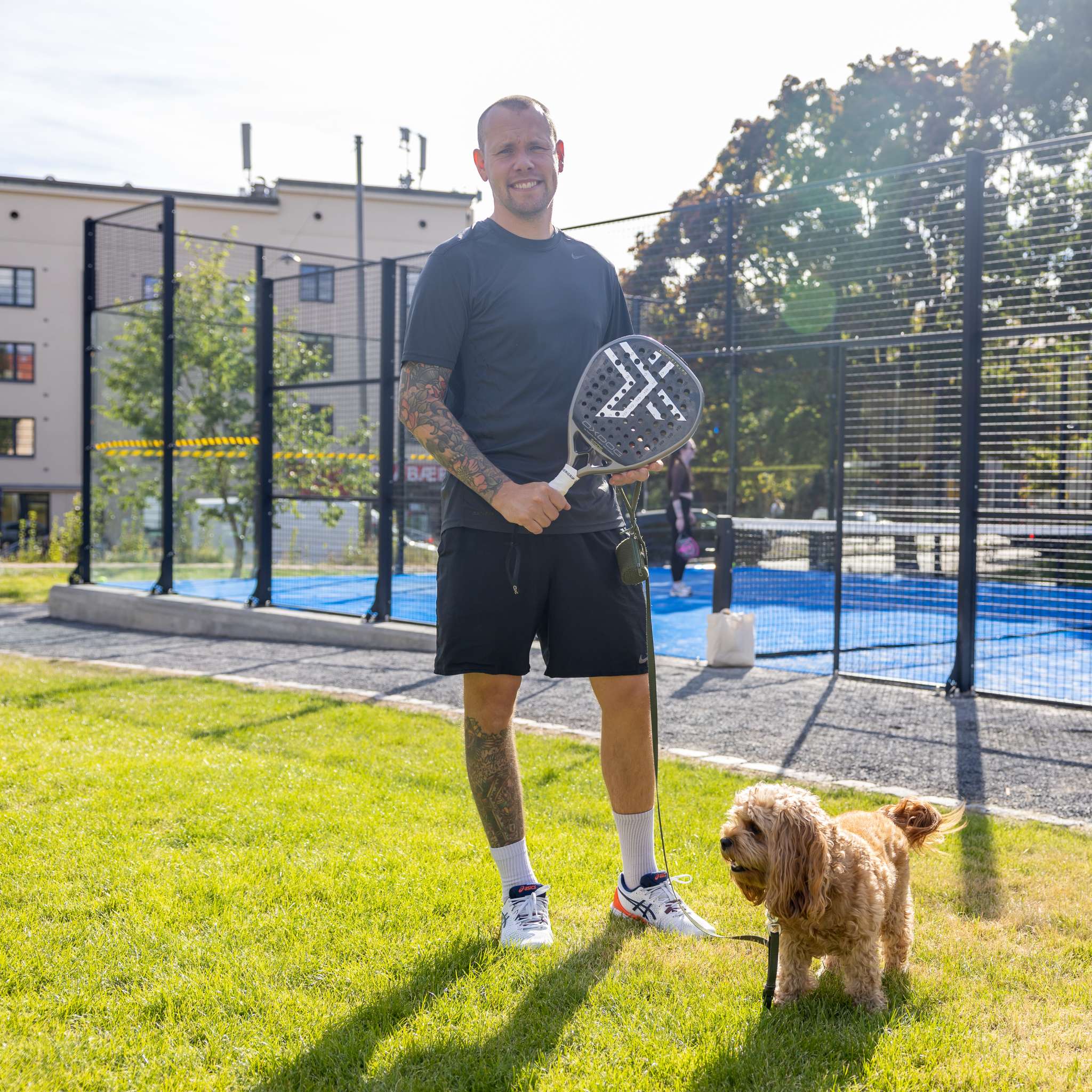Smilende mann står utenfor en padelbane. Foto.
