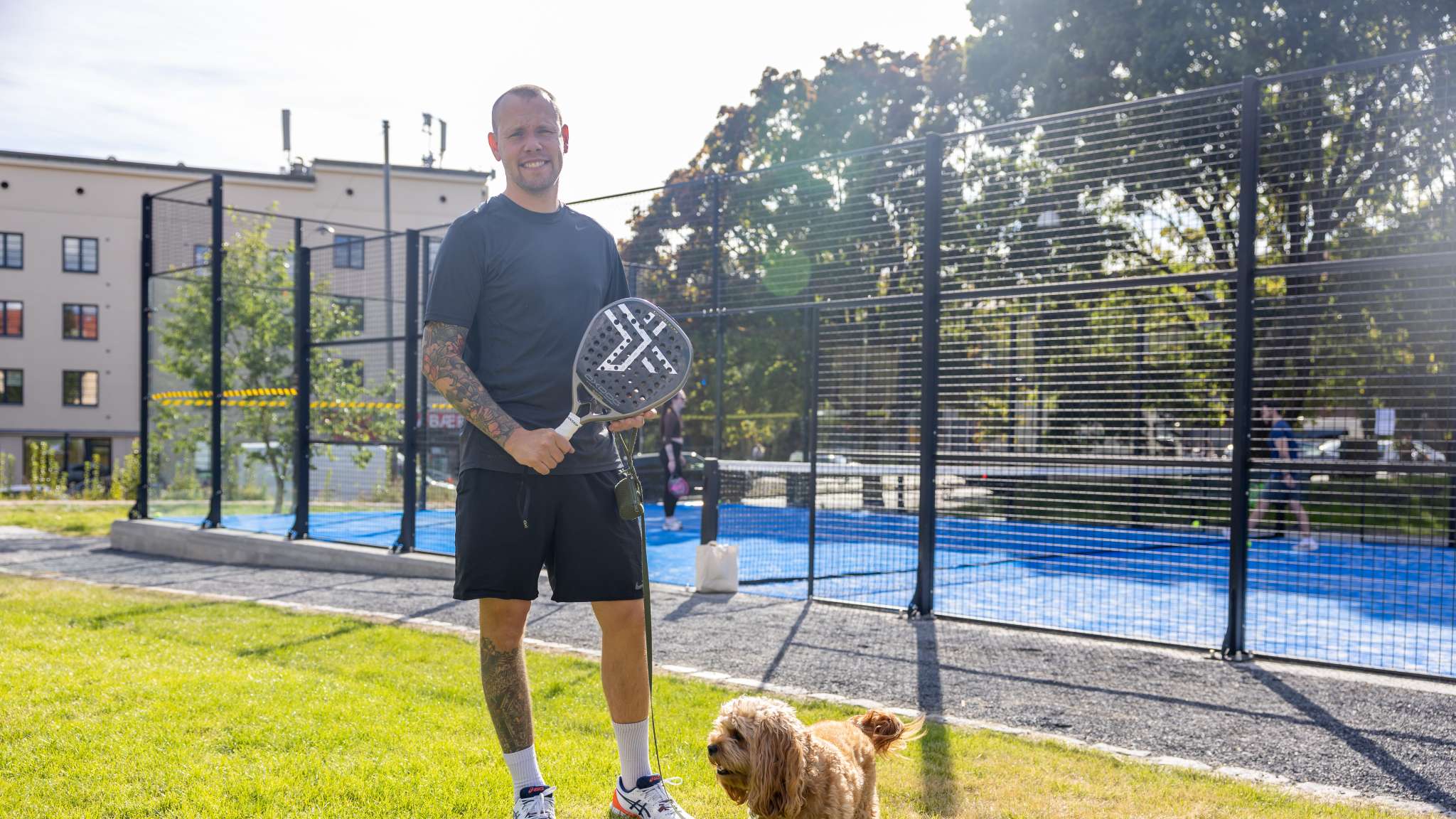 Smilende mann står utenfor en padelbane. Foto.