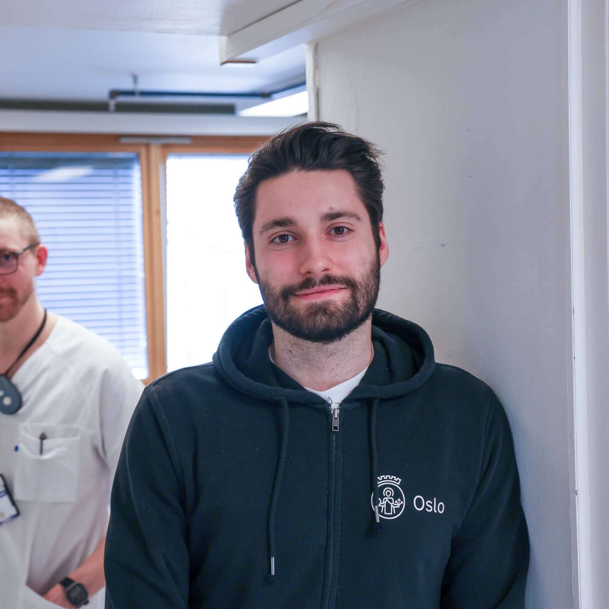En sykepleier og en utvikler ser i kamera på legevakta, foto