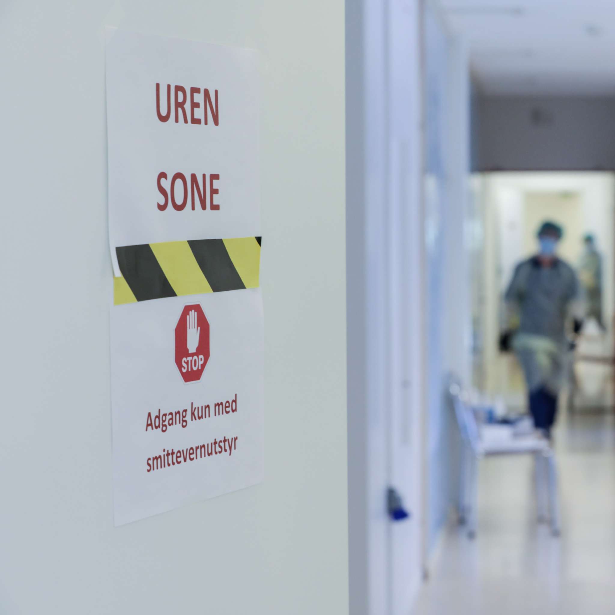 Helsearbeider i smittevernutstyr i en trappeoppgang, innenfor en dør med skiltet "Uren sone - adgang kun med smittevernutstyr"